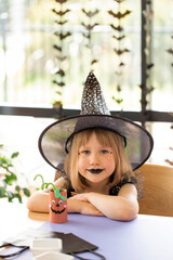 Wall Mural - A cute girl in a witch costume makes a paper craft for Halloween. Children's crafts for Halloween.