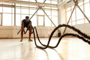 Wall Mural - sporty african american man in sportswear trains in the gym in the morning, the guy waves the ropes and does sports