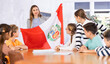 © JackF - Students sitting in class and listening carefully to female teacher holding Peru flag in hands
