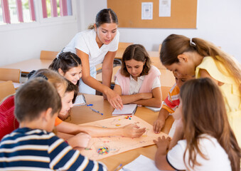 Teacher and group of kids playing board game in school after lessons. Children having fun playing interesting game.