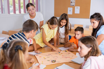 Wall Mural - Teacher and group of kids playing board game in school after lessons. Children having fun playing interesting game.