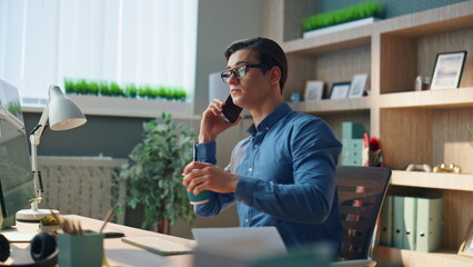 Wall Mural - Talking man drinking coffee in modern office. Freelancer speaking mobile phone