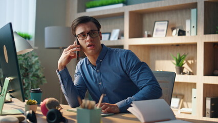Wall Mural - Positive creator talking cellphone at cabinet. Smiling designer gesturing hand