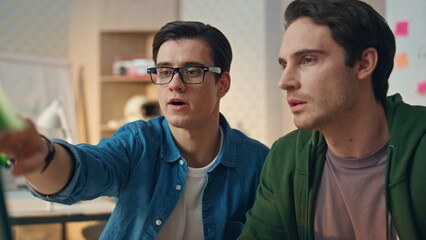 Wall Mural - Focused colleagues pointing computer office closeup. Two guys working together