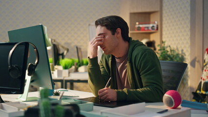Wall Mural - Tired designer rubbing eyes at computer work place. Overworked creator working