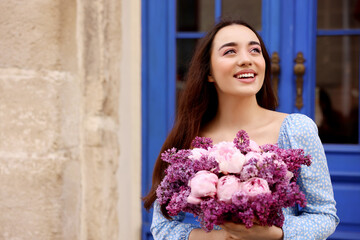 Canvas Print - Beautiful woman with bouquet of spring flowers near building outdoors, space for text