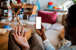 © Marko Geber - Young African American man using a smartphone with a blank screen on the couch in the living room at home