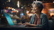 An Asian senior woman sits confidently at her desk, her face illuminated by the laptop screen. A smile crosses her face, showcasing her ease and happiness while navigating technology. Generative AI