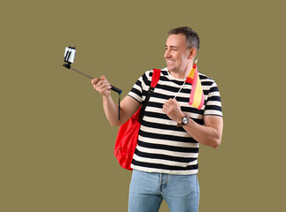 Wall Mural - Mature man with flag of Spain and backpack taking selfie on green background