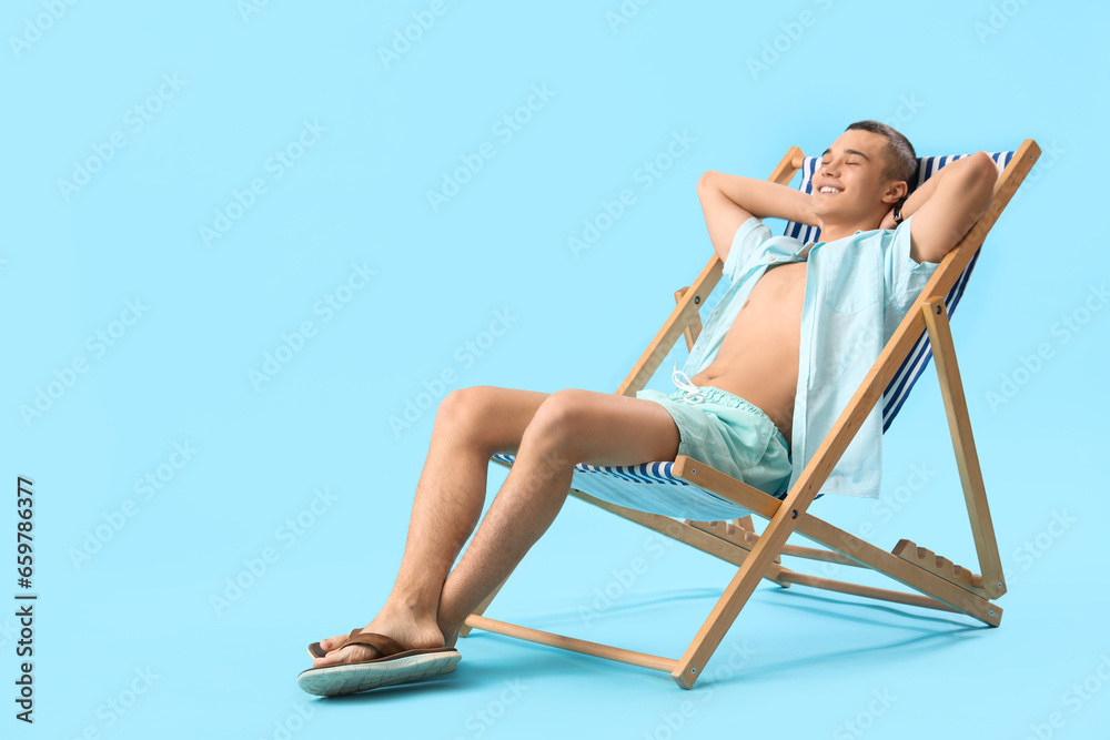 Teenage boy in deck chair on blue background