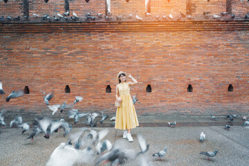 Wall Mural - Young asian woman traveler in Yellow dress with hat and bag traveling on Tha Pae Gate, Tourist visit at the old city in Chang Mai, Thailand. Asia Travel, Vacation and summer holiday concept