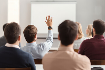 Rear view of businessman raises his hand during a presentation  at meeting in office.