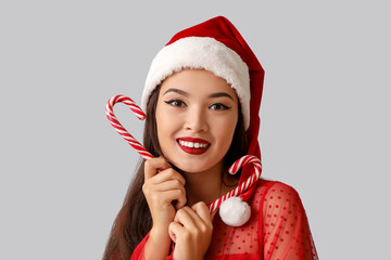 Canvas Print - Beautiful young Asian woman in Santa hat with candy canes on grey background