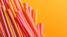 Pink, Orange, Green, And Yellow Colored Plastic Straws On An Orange Background
