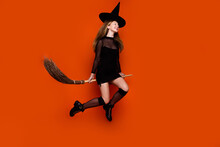 Full Size Photo Of Pretty Blonde Teenager Girl Sit Broom Fly Energetic Dressed Black Halloween Outfit Isolated On Orange Color Background