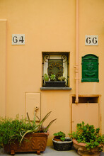 A Yellow Wall With A Green Door, Window, Mailbox And Potted Flowers. A Narrow Street In Europe