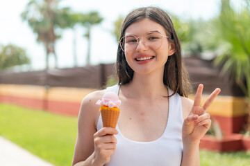 Wall Mural - Young pretty Ukrainian woman with a cornet ice cream at outdoors smiling and showing victory sign