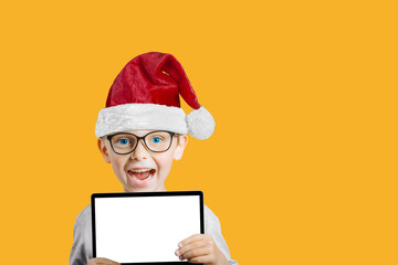 Wall Mural - a Happy child boy holding a tablet with a Santa Claus hat for Christmas