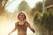 © Minet - In the backyard of house, a young girl bursts with laughter and joy as she gleefully runs through a water sprinkler on a sunny summer day