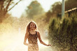 © Minet - In the backyard of house, a young girl bursts with laughter and joy as she gleefully runs through a water sprinkler on a sunny summer day