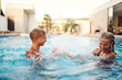 © Minet - In a sunlit modern villa, a young brother and sister joyfully splash and play in the pool, basking in the warmth of a perfect summer day