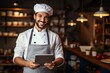 © Georgii - Portrait of young man in white chef's uniform, apron and chef's hat, with tablet in his hands. Professional restaurant kitchen worker creates original recipes and controls technological process.