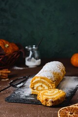 Wall Mural - Dessert, a whole pumpkin sponge roll with cream cheese cream, sprinkled with powdered sugar, on a black slate board on a brown concrete background. Pumpkin recipes.