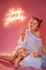 a little girl with blond hair and a little brother sits on a pink background. it's a beautiful girl'