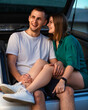 Young pretty caucasian couple kissing sitting in a trunk of their car laughing and having fun together