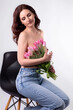 Studio portrait of a beautiful sexy slim young caucasian brunette sitting topless and in blue jeans with a bouquet of pink tulips in her hands