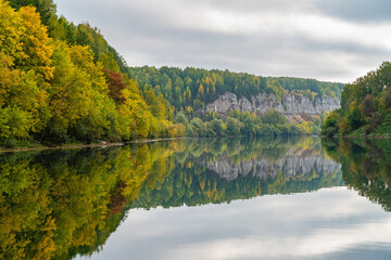 Wall Mural - autumn landscape, view of the high rocky bank of the sylva river, mirror image in the water.
