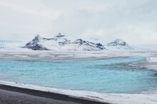 A Mesmerizing Icelandic Landscape Showcasing A Blue Lagoon, Vast Frozen Lake, Snow-covered Mountains