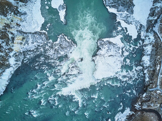  Aerial view of a majestic Icelandic waterfall surrounded by ice floes, with a crashing ocean wave and a distant iceberg.