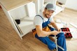 © Kostiantyn - High angle view of handyman in uniform smiling at camera while sitting on the floor and assembling drawer in kitchen