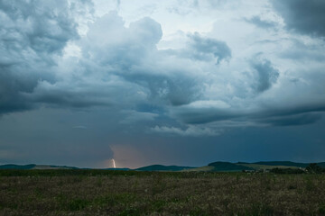 Wall Mural - a lightning bolt shoots from a distant thunderstorm cloud in the landscape of central romania