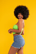 © neonshot - Young beautiful and fashionable cherful woman with afro hair, wearing casual clothes, posing over yellow studio background.