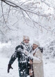 © Halfpoint - Elderly man shaking snow off the branch, laughing. Wintry landscape. Elegant senior couple walking in the snowy park.