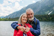 Active elderly couple hiking together in autumn mountains. Senior spouses on the vacation in the mountains celebrating anniversary. Senior tourists embrancing each other in front of lake.