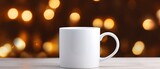 Fototapeta  - White mug on a white table with bright lights in defocus and gifts in the background. Close-up of a ceramic cup for advertising and design for New Year and Christmas.
