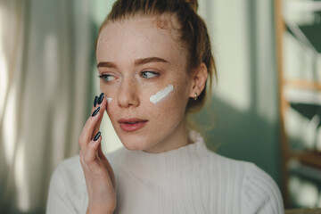 Wall Mural - attractive freckled woman lying sofa touching face with fingers using daily moisturizing cream at ho