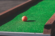 Mini golf course, process of playing miniature golf on a green artificial turf in a summer sunny day, eqipment for mini-golf in a golf club resort, club and ball