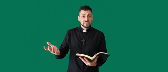 Confused priest with Bible on green background