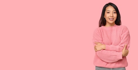 Poster - Young Asian woman hugging herself on pink background with space for text