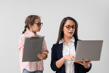 Poster - Little girl with clipboard and her working mother on light background