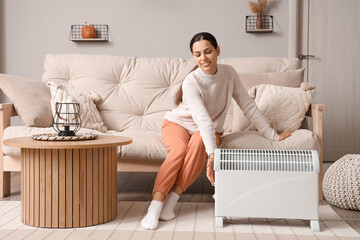 Wall Mural - Young woman warming near radiator at home