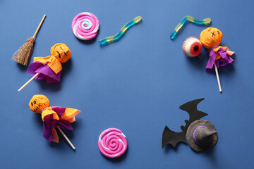 Wall Mural - Frame made of sweet lollipops with witch hat, jelly worms and eye for Halloween party on blue background