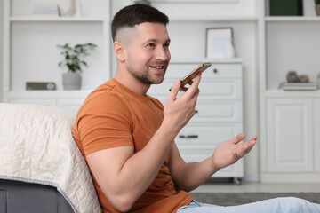 Wall Mural - Handsome man recording voice message via smartphone at home