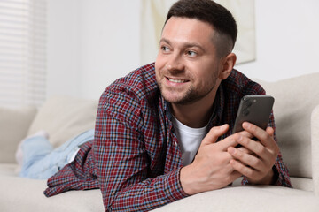 Wall Mural - Handsome man sending message via smartphone on sofa at home