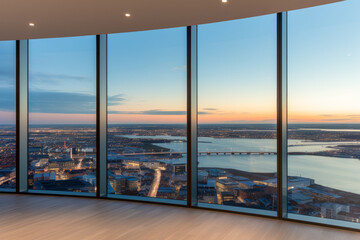 Wall Mural - View from a high-rise building overlooking a city at sunset. The view is from a room with floor-to-ceiling windows that are framed in black, and the floor is made of light-colored wood