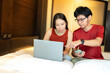 Online business owner Asian men and women working together Pointing to a laptop, there is a smartphone to check orders for company products. wearing a red shirt In the hotel bedroom